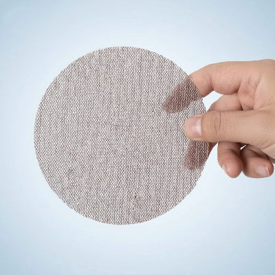 Disque abrasif sur fond bleu tenu dans une main