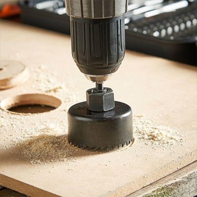 Une scie cloche installée sur une perceuse perçant un trou dans une planche