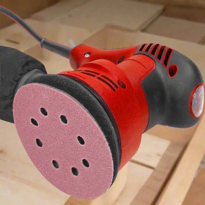Ponceuse excentrique rouge montrant le plateau de rotation avec du papier sablé à huit trous pour le bois 