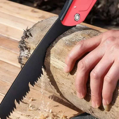 Scie pliante rouge utilisée pour couper une bûche